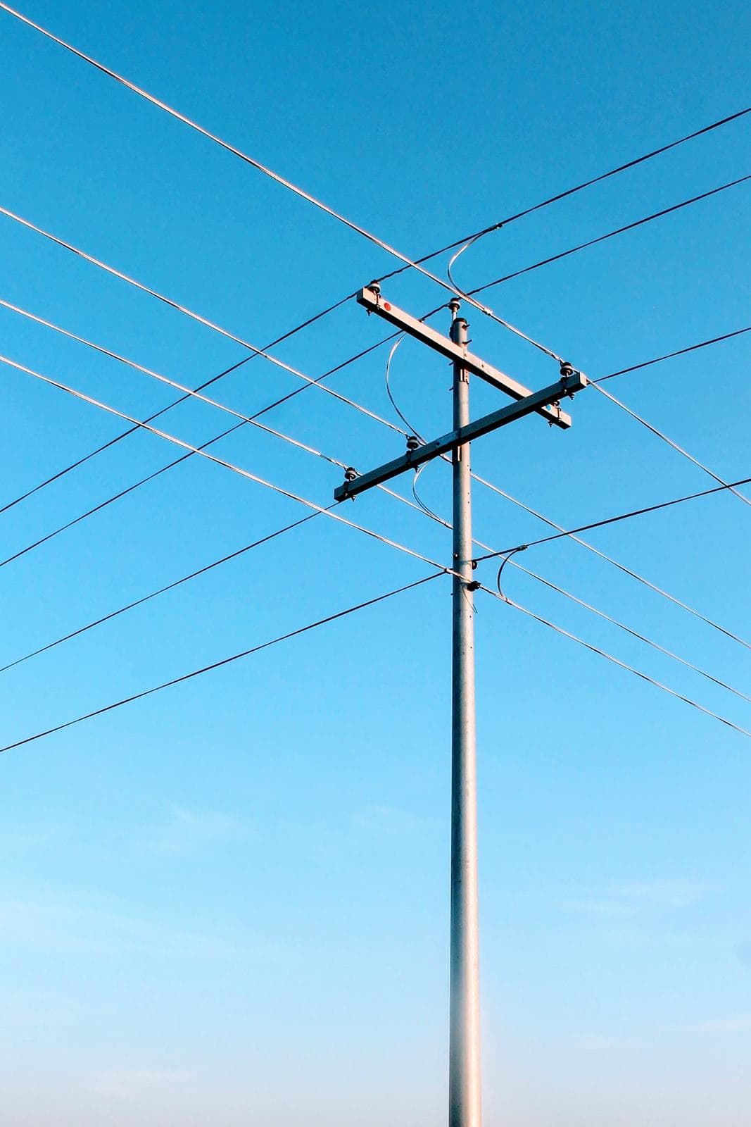 Overhead distribution pole with crossarm, insulators and conductors against a clear sky.